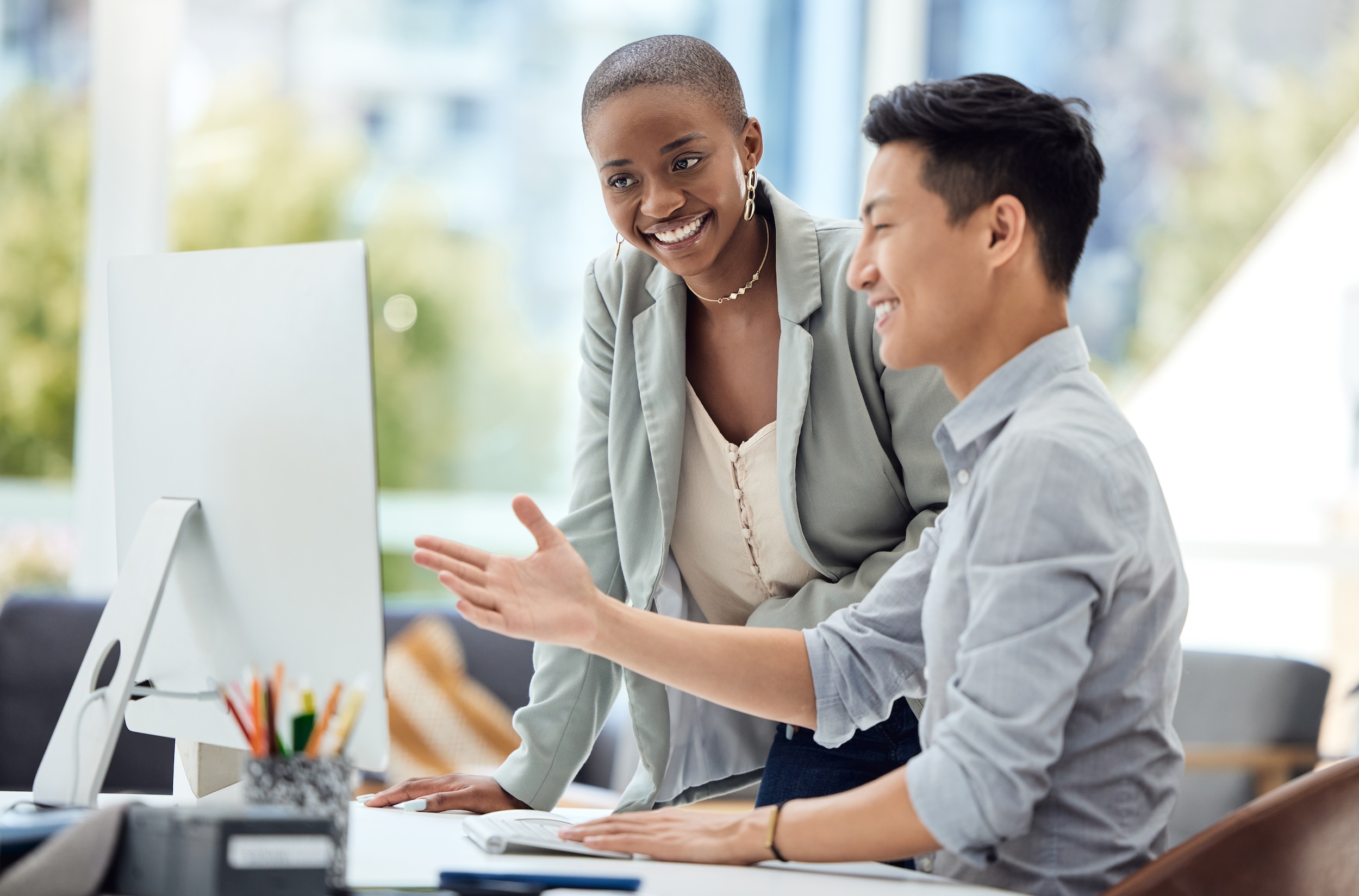 IT Consulting between an asian businessman and black woman, standing around a computer collaborating.